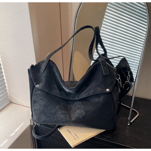 Detail of black tote bag showing embossed daisy floral pattern and smooth matte leather