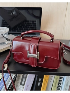 Close-up of glossy wine red leather handbag with silver metal buckle on a desk