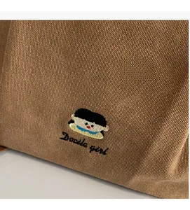 Close-up of intricate girl embroidery and Docile girl text on brown canvas tote bag
