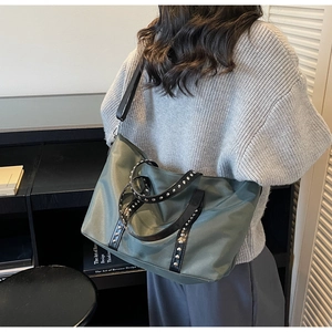 Detail of dark green nylon tote bag with silver studs and black leather trim