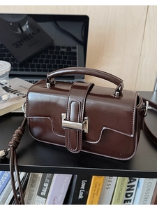Detail view of glossy chocolate brown crossbody bag with silver buckle on desk