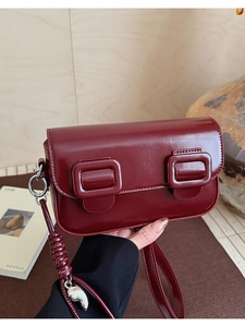 Detail of burgundy saddle bag showing glossy texture, double buckles and heart charm