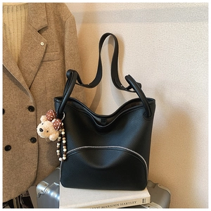 Detail of black pebbled tote bag with curved zipper and cute plush bear accessory