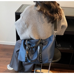 Detail view of navy nylon tote bag featuring silver rivet trim and adjustable strap