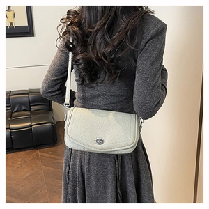 Detail of a creamy white pebble leather crossbody bag with a silver swivel lock closure