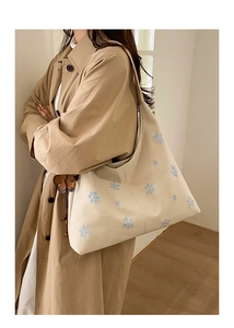 Detail of cream tote bag with blue snowflake embroidery on durable canvas fabric