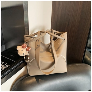 Detail of beige tote bag in lychee leather featuring a plush bear charm and dual handles