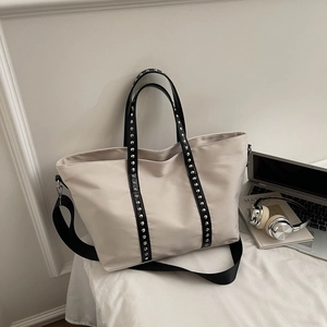 Close-up of beige tote bag with black rivet straps, wide strap, and laptop on desk