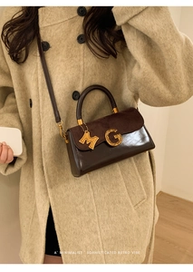Detail of brown leather handbag with gold letter G buckle and M charm on beige coat