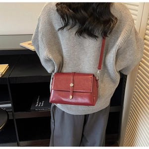 Close-up of burgundy leather crossbody bag with silver buckle worn over a grey sweater
