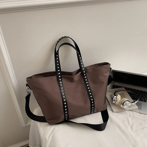 Close-up of brown tote bag with silver studs on black leather handle and wide shoulder strap