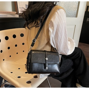 Side view of a model wearing a black square leather crossbody bag with silver buckle