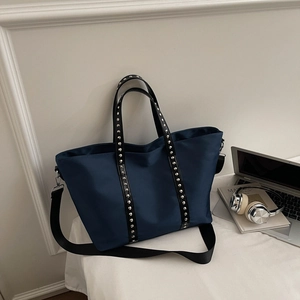 Close-up of navy nylon tote bag showing silver rivets on black straps and zipper detail