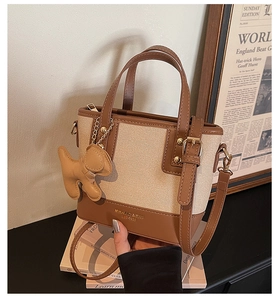 Detail of canvas bucket bag with leather trim, featuring a dog charm and long strap