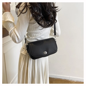 Detail of black pebbled leather shoulder bag featuring a silver oval metal turn-lock closure