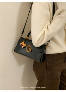 Close-up of black glossy handbag featuring a gold textured G clasp and M charm