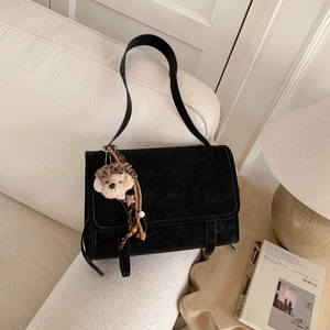Close-up of black suede crossbody bag with cute plush puppy charm on a sofa