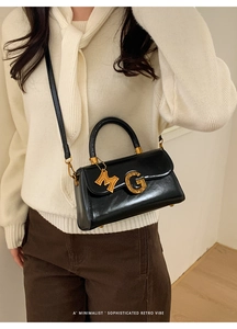Close-up of retro black glossy leather handbag with gold G buckle and M tag