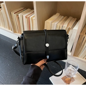 Detail of a minimalist black square bag on a wooden desk with a silver metal buckle