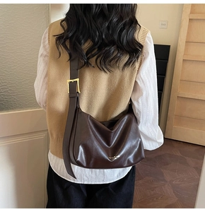 Détail du sac bandoulière en cuir marron foncé souple avec sangle large et boucle dorée