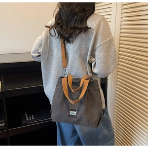 Detail of dark grey canvas tote bag featuring boy embroidery and brown crossbody strap