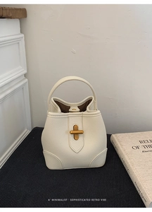 Close-up of beige bucket bag with lychee texture and gold metal twist lock buckle
