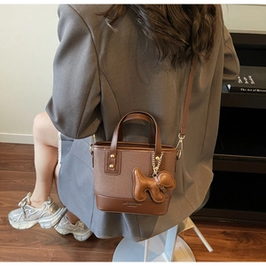 Brown leather bucket bag detail with dog charm and adjustable strap worn with a blazer