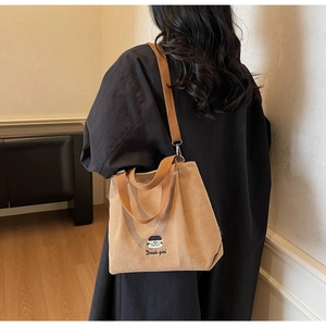 Detail of light brown corduroy shoulder bag featuring cute girl embroidery and long straps