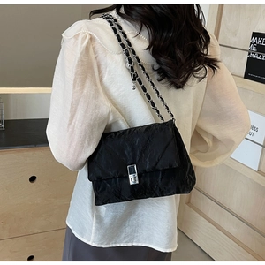 Detail of black quilted crossbody bag with chain strap and metallic clasp on a model