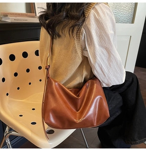 Détail d'un sac à bandoulière en cuir marron souple avec logo doré et sangle réglable
