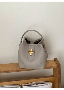 Detail of grey lychee leather bucket bag featuring a golden cross-shaped twist lock