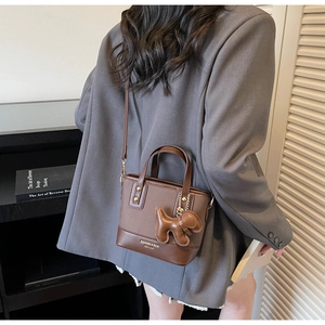 Detail of brown leather bucket bag featuring a decorative dog charm and golden hardware