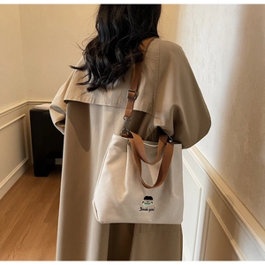 Detailed view of off-white canvas tote bag with brown straps and cute girl embroidery