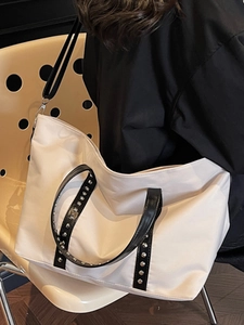 Fashionable off-white tote bag with black rivet straps and long adjustable shoulder strap
