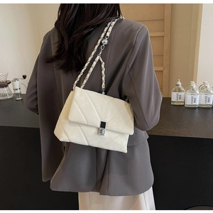 Detail of a white chevron quilted shoulder bag with silver chain strap and metal lock