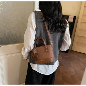 Detail of dark brown leather bucket bag with gold studs and a decorative bow charm
