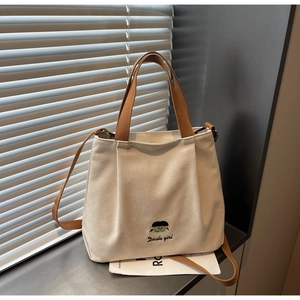 Detail of embroidered beige canvas tote bag with brown straps in soft natural sunlight