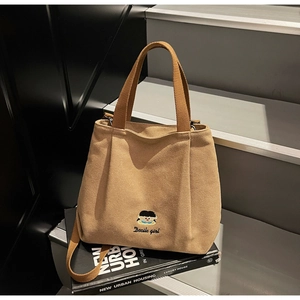 Detail of embroidered khaki canvas tote bag on books with adjustable shoulder strap