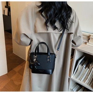 Detail of minimalist black crossbody bucket bag with dog charm on beige trench coat