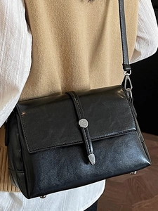 Vintage black leather crossbody bag with silver buckle detail on a beige knit vest