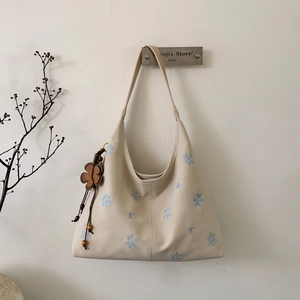 Detail of beige hobo bag with blue snowflake embroidery and floral charm pendant