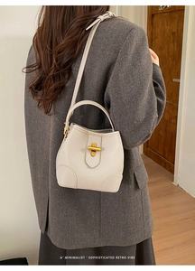 Close-up of minimalist cream leather bucket bag texture and golden T-bar clasp detail