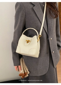Detail of white bucket bag with lychee pattern and golden buckle on grey blazer