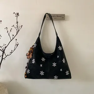 Detail of black suede tote bag with white snowflake embroidery and flower charm hanging