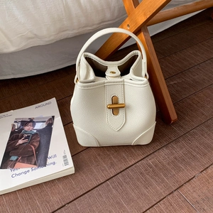 Detailed macro view of white pebble leather texture and gold T-shaped clasp on bucket bag