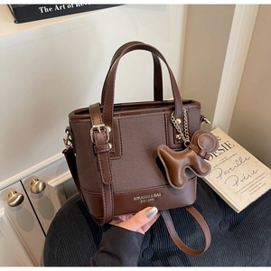 Close-up of brown canvas and leather bag with dog charm and gold hardware detail