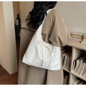 Side view of white large crescent tote bag with oversized bow on a camel trench coat