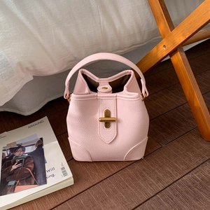 Detailed close-up of light pink bucket bag with golden twist lock on wooden floor