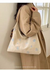 Detail view of beige tote bag with blue snowflake embroidery and wood bead tassel charm