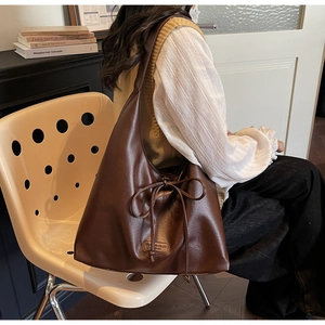 Deep brown tote bag with vintage matte leather texture and bow detail in lifestyle setting